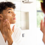 Teenage boy applying cream to sensitive skin on his face